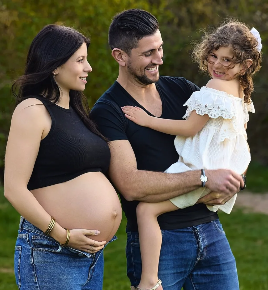 Une famille en extérieur : maman enceinte, papa et leur fille qui rit dans ses bras