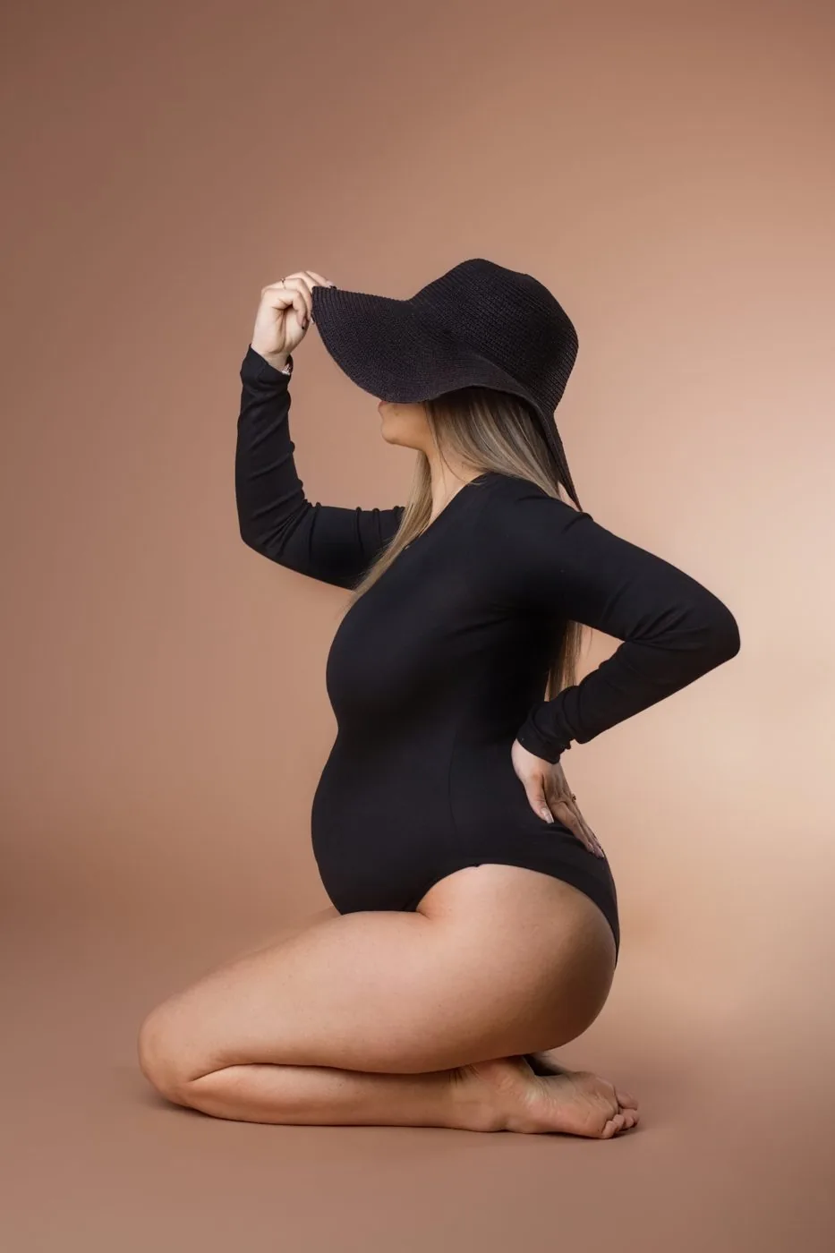 Future maman de profil en body noir et grand chapeau