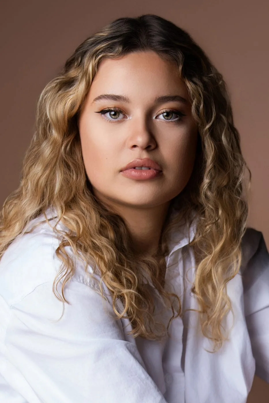 Portrait studio éditorial d'une jeune femme aux cheveux bouclés, chemise blanche, fond terracotta