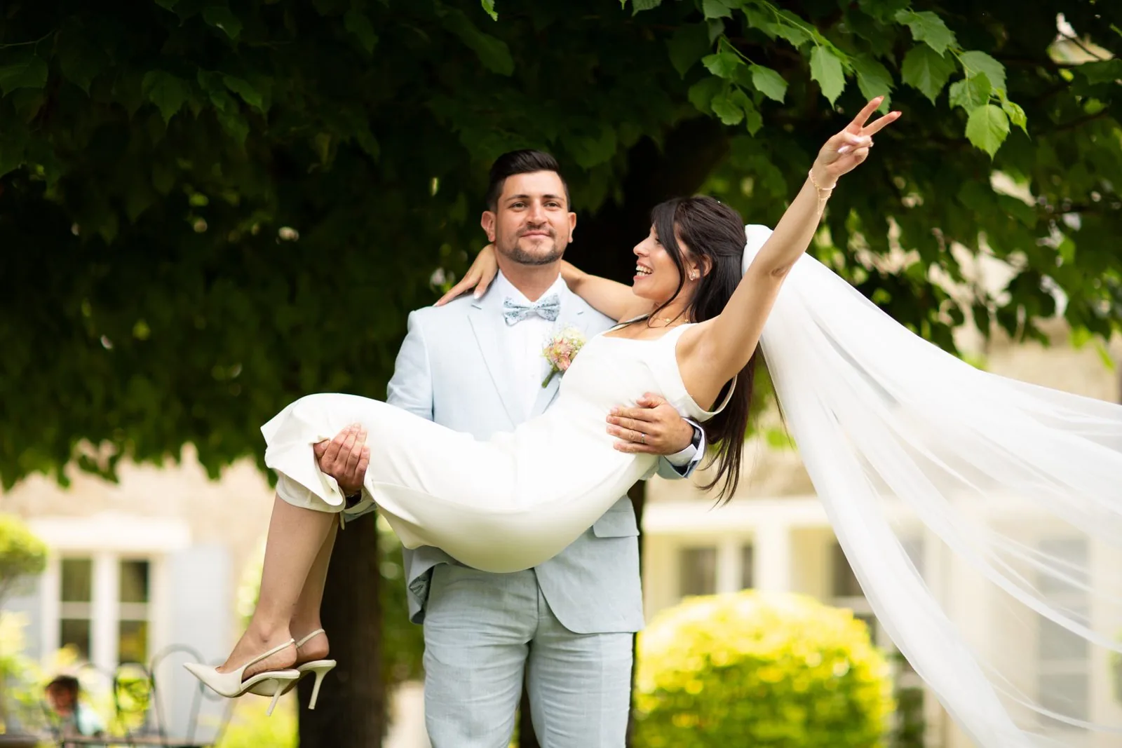 Le marié porte la mariée dans ses bras, voile au vent