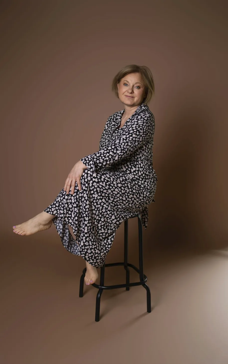 Femme assise sur un tabouret, robe fleurie, pieds nus