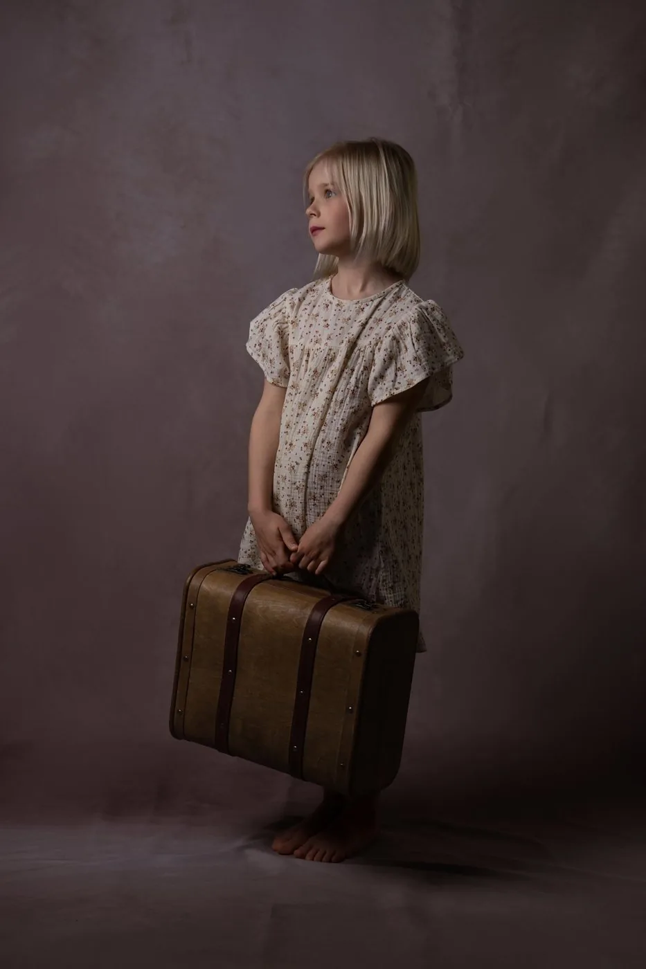 Fillette en robe à fleurs avec une valise ancienne