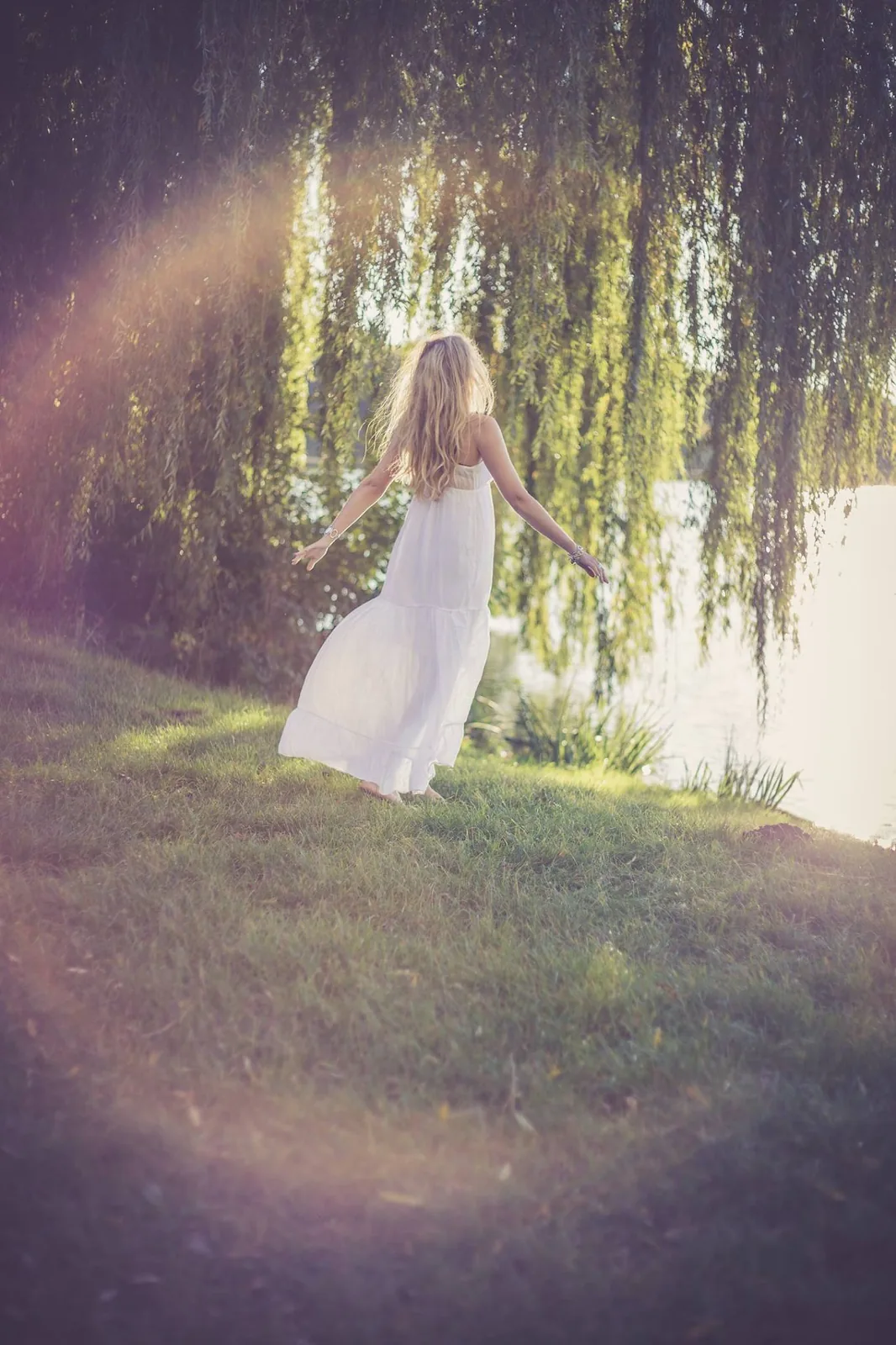 Jeune femme de dos qui danse sous un saule, robe blanche